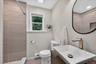 Lower-level full bathroom, Modern bathroom featuring a rectangular vessel sink, wood-finish vanity, large oval mirror, tiled shower with recessed shel