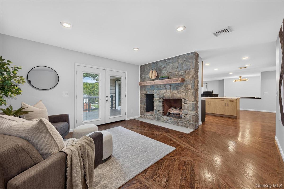 Stone fireplace with wood mantel, recessed ceiling lighting, French doors, wood-finish flooring, and light-toned cabinetry