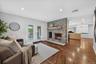 Stone fireplace with wood mantel, recessed ceiling lighting, French doors, wood-finish flooring, and light-toned cabinetry