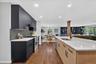 Modern kitchen featuring a large island with an undermount sink, stainless steel appliances, dark cabinetry, and wood-finish flooring