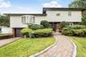 Split-level home featuring a brick paver walkway, mature shrubbery, a bay window, and a brown garage door