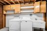 Utility room with exposed ceiling joists, light wood-finish cabinetry, open shelving, and a utility sink