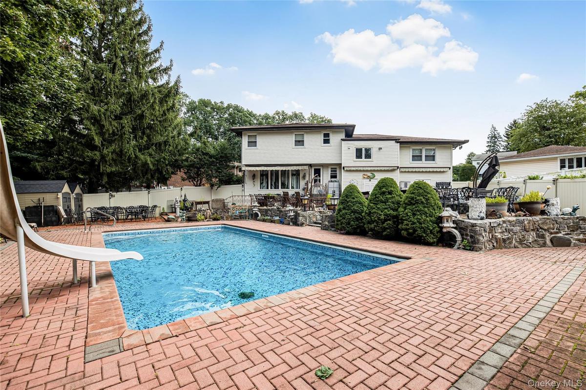 Swimming pool with a water slide, surrounded by a brick paver patio and privacy fencing