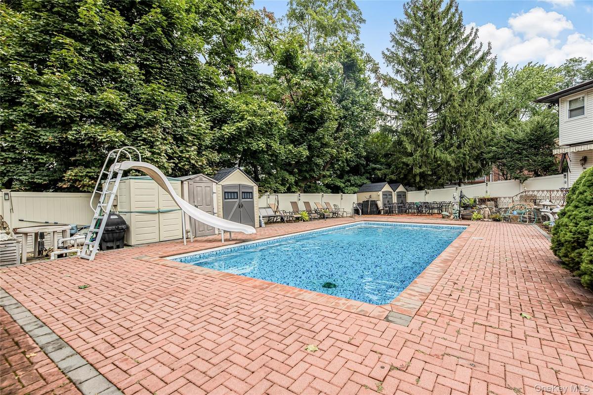 Swimming pool with a water slide, surrounded by a brick paver patio and privacy fencing
