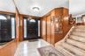 Foyer featuring a black entry door with decorative glass sidelights, tile flooring, wood paneling, and a staircase with an integrated runner
