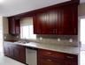 Rich wood cabinetry with decorative archway, light-toned countertop, stainless steel sink, stainless steel dishwasher, and tiled flooring