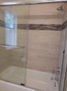 Bathtub with chrome fixtures, full-height tile surround, decorative tile accent band, and clear glass sliding shower doors