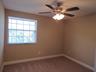 Carpeted flooring, neutral wall tones, multi-pane window, ceiling fan with integrated lighting, and white baseboards