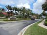 Main entrance featuring a custom "Ventura" sign, lush tropical landscaping with mature palm trees, a dedicated entry road, and a security booth