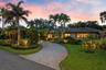 Paver driveway, lush landscaping, mature palm trees, exterior lighting, and a tile roof