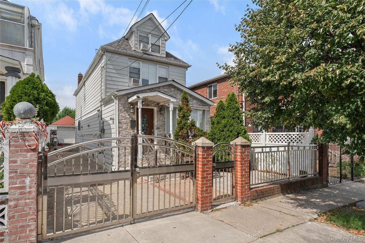 Stone-clad facade with covered entry, dual driveway gates, and brick-columned fencing