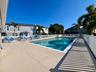 Community swimming pool with surrounding fencing, concrete pool deck, and palm trees