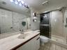 Vanity with integrated sink and chrome faucet, full-width mirror with vanity lighting, white paneled cabinetry, tiled flooring, and a glass-enclosed s