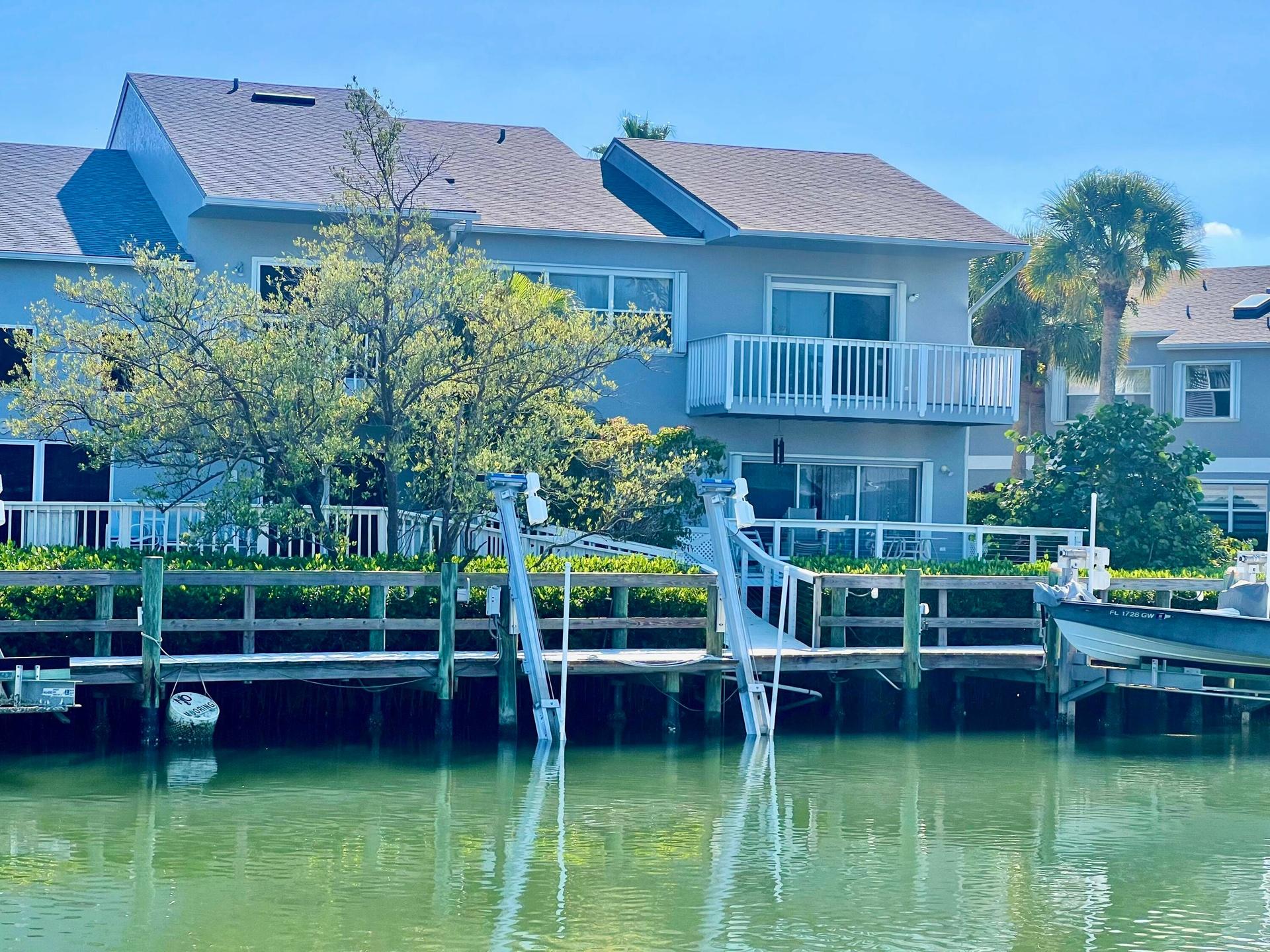 Waterfront property featuring a private boat dock, boat lift, water-facing balcony, and ground-level patio