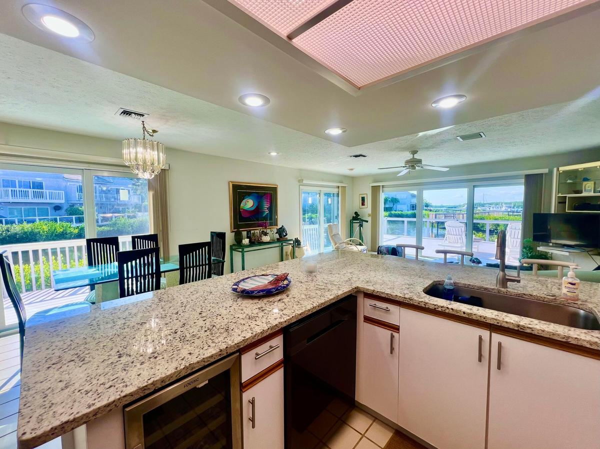 Large L-shaped kitchen island with integrated sink, under-cabinet wine refrigerator, and light-toned countertops