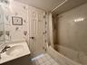 Vanity with integrated sink and countertop, textured wallpaper, tile flooring, built-in bathtub with shower, and multi-panel door