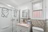 Updated full bathroom featuring a glass-enclosed shower, modern vanity, tile backsplash, and natural light. 1st Floor