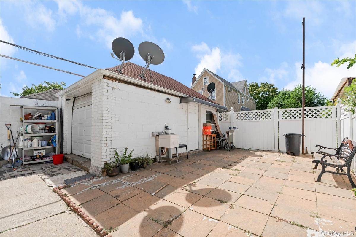 Detached white brick garage with a roll-up door, paved patio, and white lattice fencing