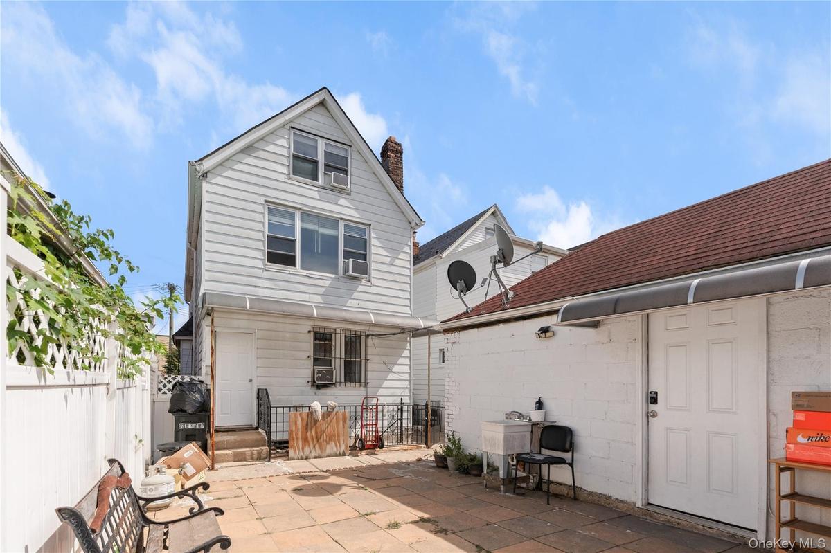 Paved patio area, white exterior siding, gabled roofline, security bars on windows, attached garage structure