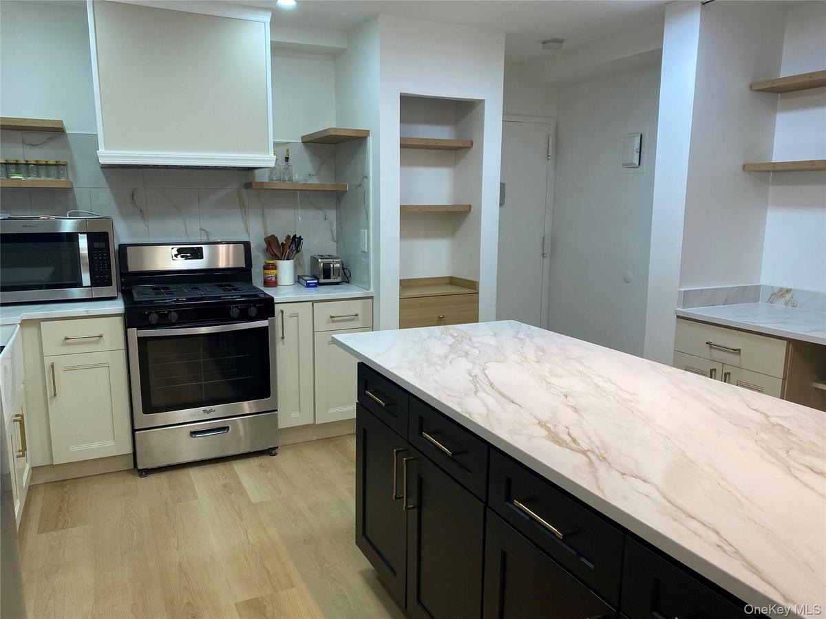 Kitchen featuring a central island with a light-toned countertop, stainless steel range, white cabinetry, and wood-finish flooring