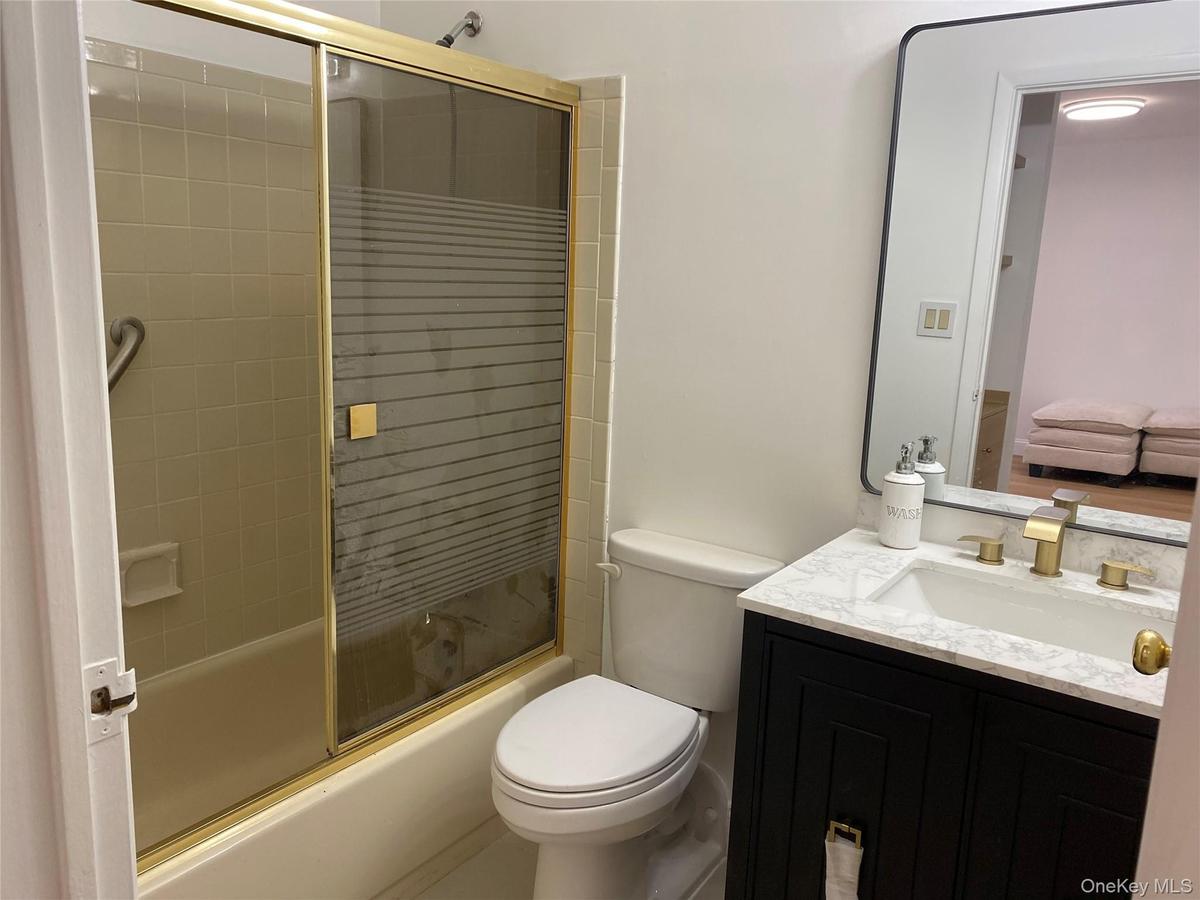Tub/shower combination with gold-toned sliding glass door, white tile wall surround, and grab bar