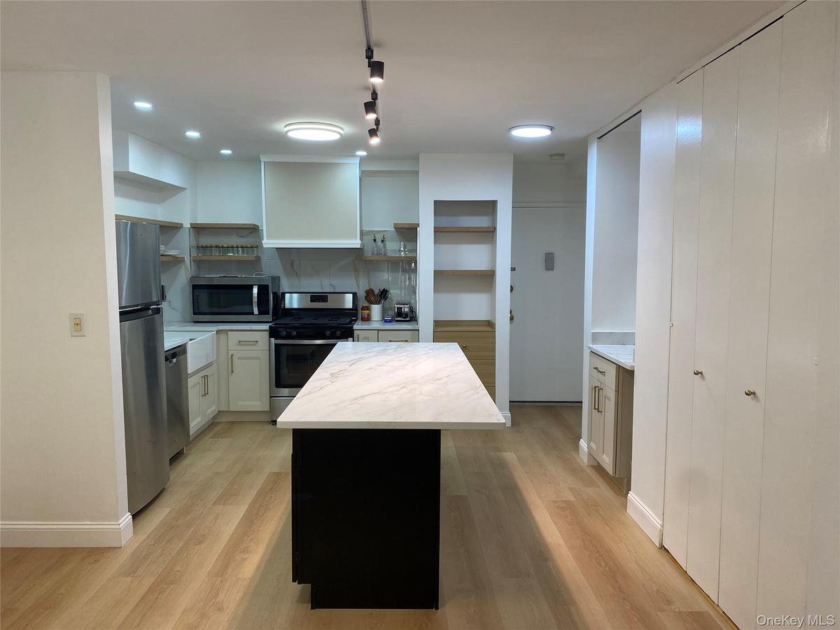 Kitchen featuring wood-finish flooring, stainless steel appliances, a center island with a white countertop, recessed lighting, and white cabinetry