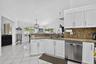 Bright, open kitchen featuring white cabinetry, granite countertops, stainless steel appliances including a dishwasher, pendant lighting, ceiling fan,