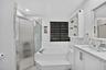 Built-in bathtub with integrated steps, frosted glass shower enclosure, white vanity with integrated sink, stone-finish countertop, and wall-mounted s