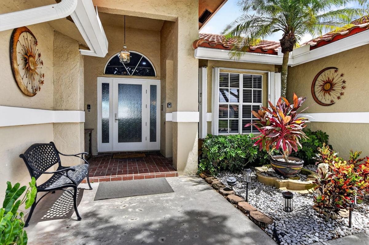 Arched transom window above double entry doors with frosted glass panels, brick-finish flooring at entry, window with white blinds, mature palm tree, 