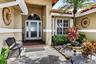 Arched transom window above double entry doors with frosted glass panels, brick-finish flooring at entry, window with white blinds, mature palm tree, 