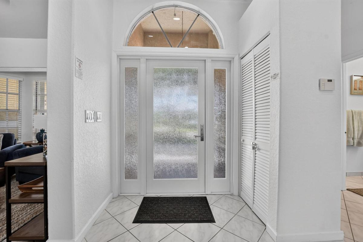 Entryway featuring a decorative arched transom window, frosted glass paneled door with side panels, louvered closet doors, and diagonal tile flooring