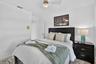 Recessed lighting, wood-finish flooring, ceiling fan, dark wood headboard, and bedside table with storage