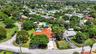 Aerial view showcasing a substantial corner-lot property with a clay tile roof, mature landscaping throughout the grounds, a sparkling swimming pool w