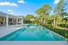 Expansive outdoor area featuring an infinity-edge pool with light-colored coping, a covered patio with a built-in outdoor kitchen, and tropical landsc