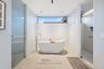 Freestanding soaking tub with floor-mounted faucet, frosted glass shower enclosure, and transom window