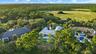 Lush green landscaping with mature trees, expansive wetland scenery, and a visible swimming pool