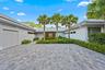 Elegant driveway featuring permeable pavers in a geometric pattern, bordered by lush tropical landscaping with mature palm trees and manicured hedges