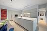 Integrated kitchen featuring a large central island with sink, ample light-grey cabinetry, stainless steel built-in appliances, and light wood-finish 
