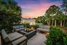 Paver patio with a built-in fire pit, lush landscaping, and mature palm trees