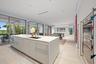 Contemporary kitchen anchored by a white cabinetry island with waterfall countertop, stainless steel appliances, and light wood-finish flooring