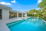 Resort-style saltwater swimming pool with turquoise finish and generous sun deck, anchored by a modern white pergola structure and expansive covered l