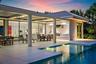 Modern residence featuring a resort-style backyard with an illuminated saltwater pool, expansive travertine-finish patio, and seamless indoor-outdoor 