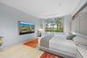 Recessed wall-mounted television, full-height sliding glass doors, built-in headboard, wood-finish flooring, and integrated ceiling lighting