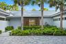 Modern residence featuring a clean-lined white exterior with standing-seam metal roofing, framed by three mature palm trees