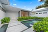 Architectural exterior with white stucco finish, wood slat detailing, metal roof, and rectangular transom windows