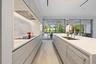 Modern kitchen featuring white flat-panel cabinetry, light wood-finish flooring, a stainless steel sink, and a cooktop with an integrated range hood
