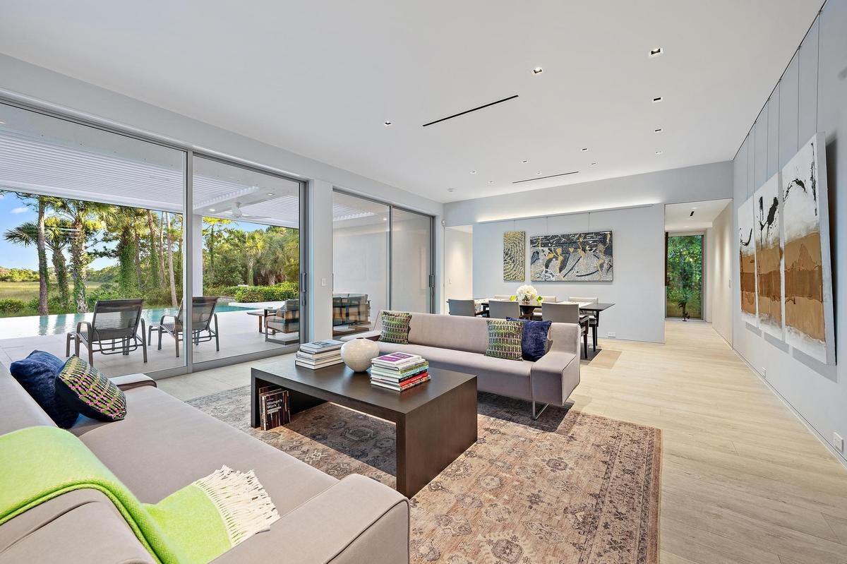 Sophisticated open-concept living space featuring floor-to-ceiling sliding glass doors opening to expansive outdoor grounds, light wood-finish floorin