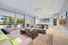 Sophisticated open-concept living space featuring floor-to-ceiling sliding glass doors opening to expansive outdoor grounds, light wood-finish floorin