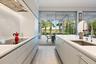 Modern kitchen featuring white cabinetry with handleless design, quartz countertops, stainless steel undermount sink with contemporary faucet, and int