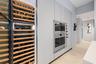 Integrated wine refrigerator with wood racks, built-in double ovens with stainless steel finishes, light wood-finish flooring, and minimalist flat-pan